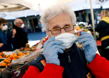 Owner of a fruit stall at Campo de' Fiori market adjusts a protective face mask on the second day of an unprecedented lockdown across all of the country, imposed to slow the outbreak of coronavirus, in Rome, Italy March 11, 2020. REUTERS/Guglielmo Mangiapane