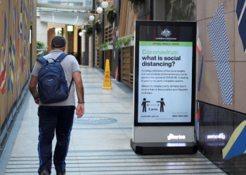 A man walks in a corridor near a sign with instructions about the coronavirus and social distancing following the implementation of stricter social-distancing and self-isolation rules to limit the spread of the coronavirus disease (COVID-19) in Sydney, Australia, March 31, 2020. REUTERS/Loren Elliott