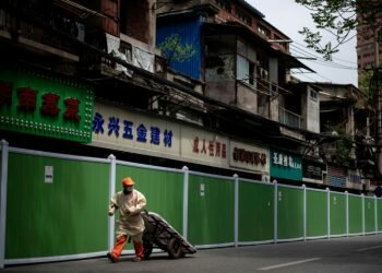 A worker pulls a cart as he walks beside a barricade in Wuhan, on April 14, 2020.PHOTO: AFP
