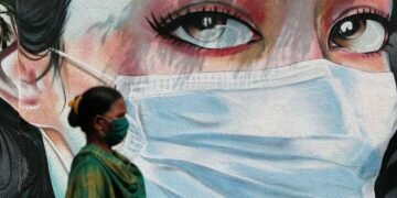 © Reuters/FRANCIS MASCARENHAS A woman walks past a graffiti of a girl wearing a protective mask amidst the spread of the coronavirus disease (COVID-19) in Mumbai