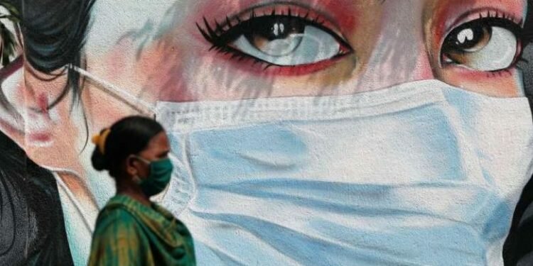 © Reuters/FRANCIS MASCARENHAS A woman walks past a graffiti of a girl wearing a protective mask amidst the spread of the coronavirus disease (COVID-19) in Mumbai