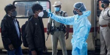 FILE PHOTO: A health worker in personal protective equipment (PPE) checks the temperature of passengers at a railway station, amid the spread of the coronavirus disease (COVID-19), in Mumbai, India November 27, 2020. REUTERS/Francis Mascarenhas/Files