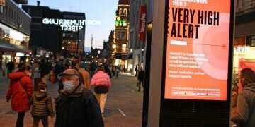 © Oli SCARFF / AFP A pedestrian wearing a face mask or covering due to the COVID-19 pandemic, walks past an information board displaying information on Tier 3 rules to combat the spread of the coronavirus.