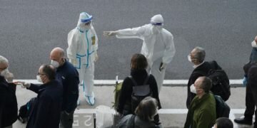 A worker in protective coverings directs members of the World Health Organization (WHO) team on their arrival at the airport in Wuhan in central China's Hubei province on Thursday, Jan. 14, 2021. Image credits - NG HAN GUAN, AP